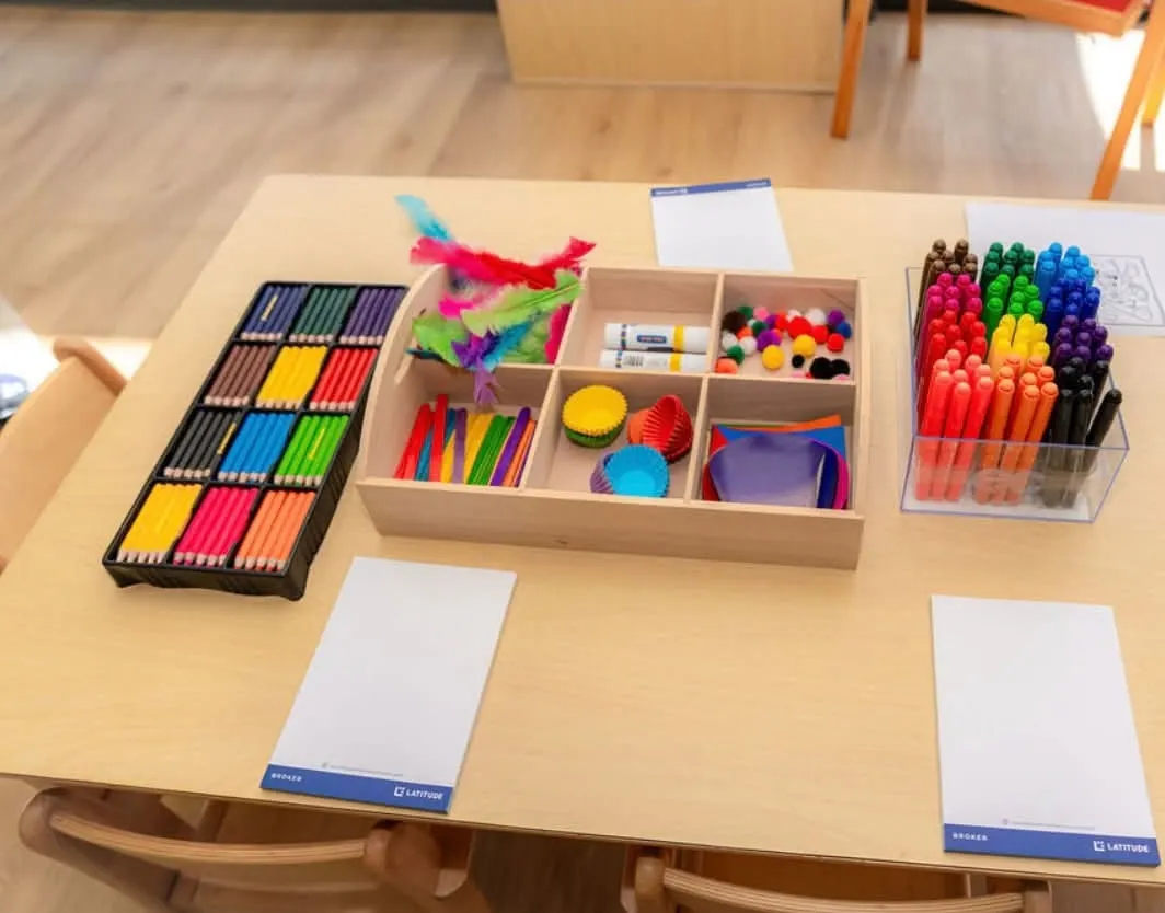 Art table set with coloured pencils, markers, feathers, pom-poms and paper