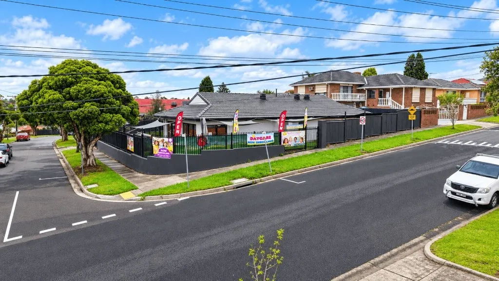 YoMySunshine childcare centre on a corner in Dandenong North, with a dark fence, shade sails and a now enrolling banner