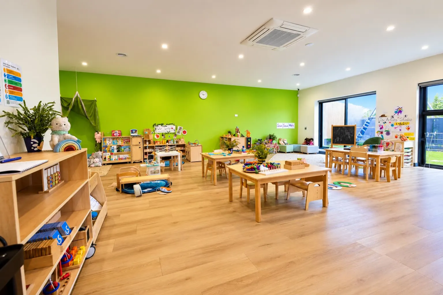 Large green learning room at YoMy Sunshine with timber tables, open shelves and windows onto the play area