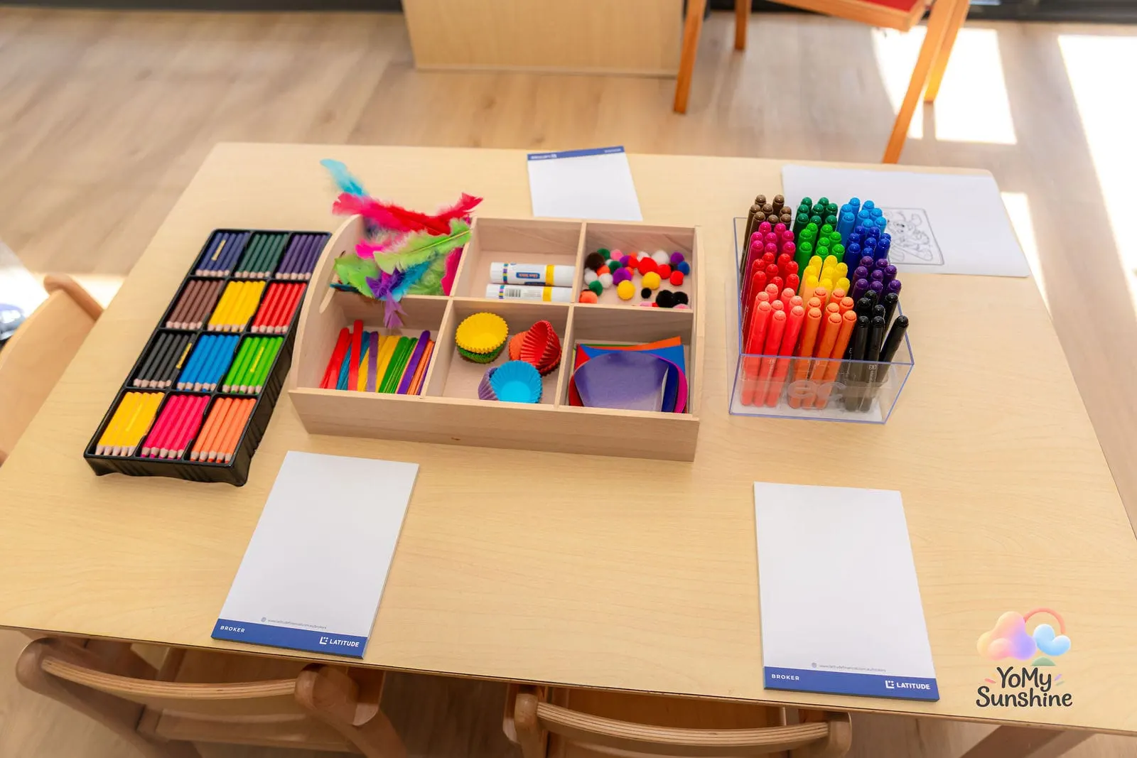 Art table set with coloured pencils, markers, feathers and craft trays, ready for play
