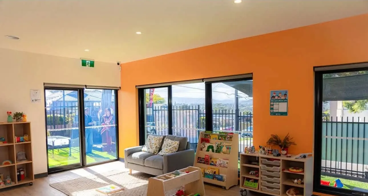 Play room with a grey couch, woven rug, picture-book display and low toy shelves beside sliding doors to the garden