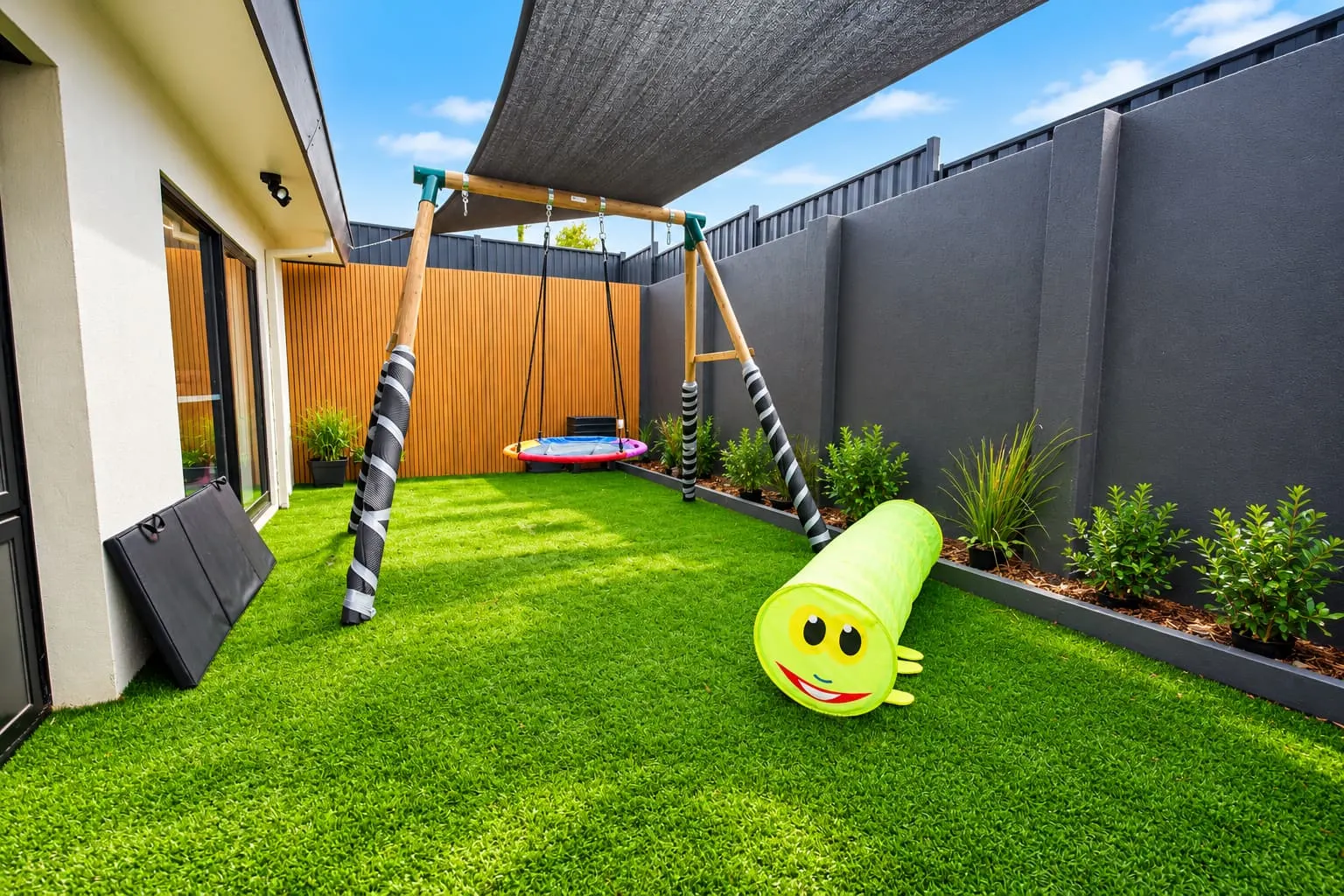 Shaded outdoor play area with a swing, a play tunnel and artificial grass