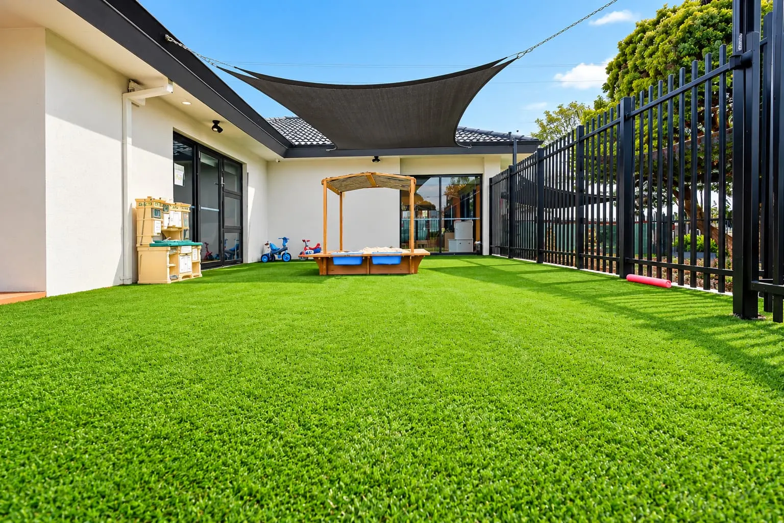 Fenced outdoor play area with artificial grass and shade sails
