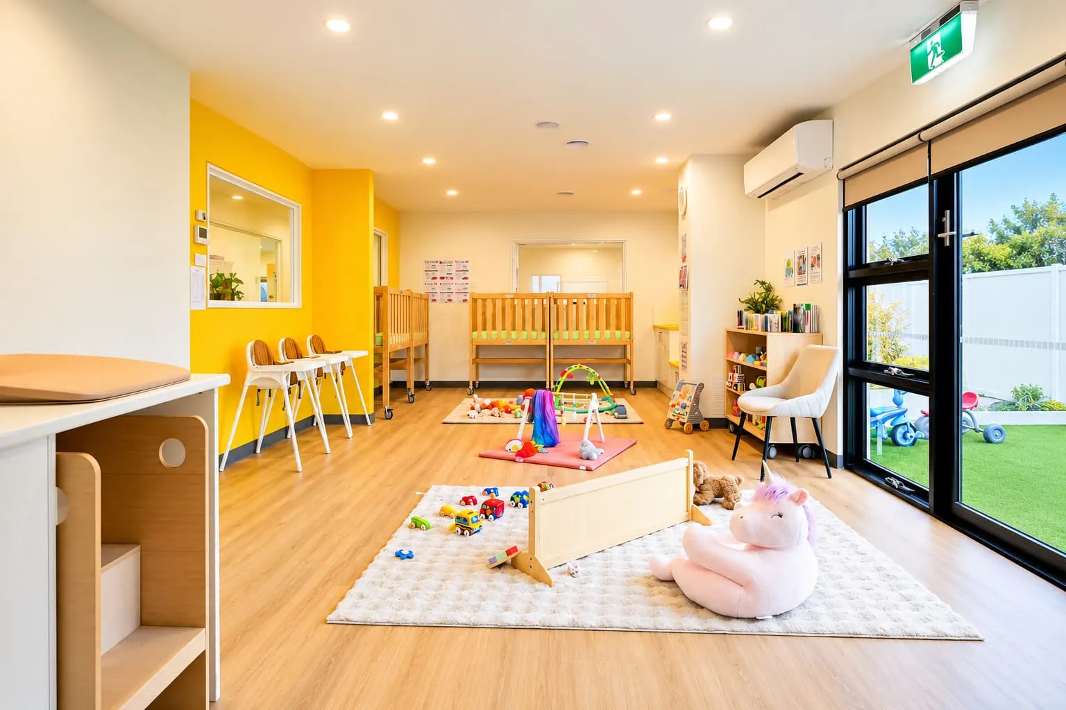 Yellow nursery room with low shelves, soft toys and windows looking onto the outdoor play area